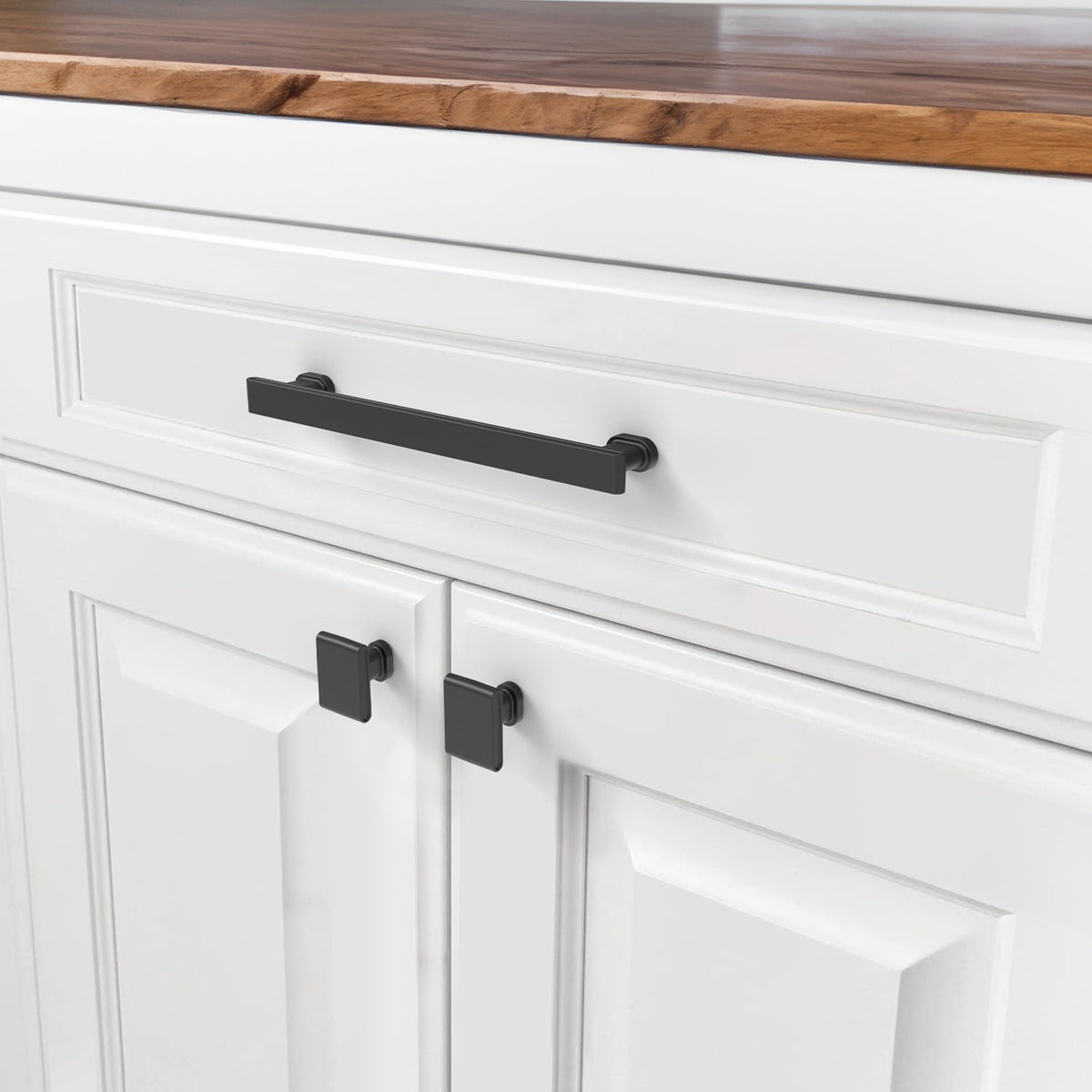 Black bar pull and square knobs installed on white cabinet doors and drawer