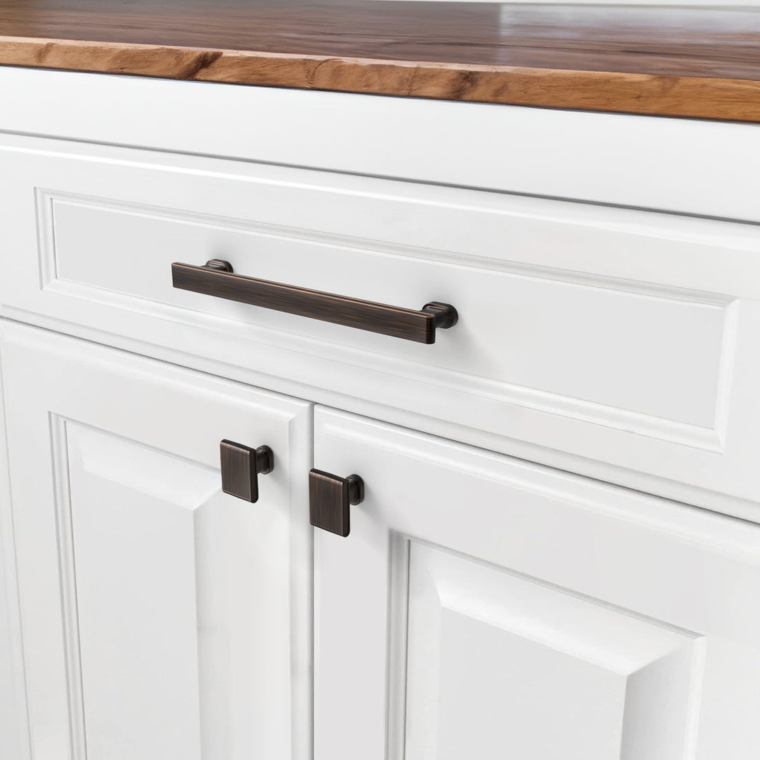 Oil rubbed bronze bar pull and square knobs installed on white cabinet doors and drawer